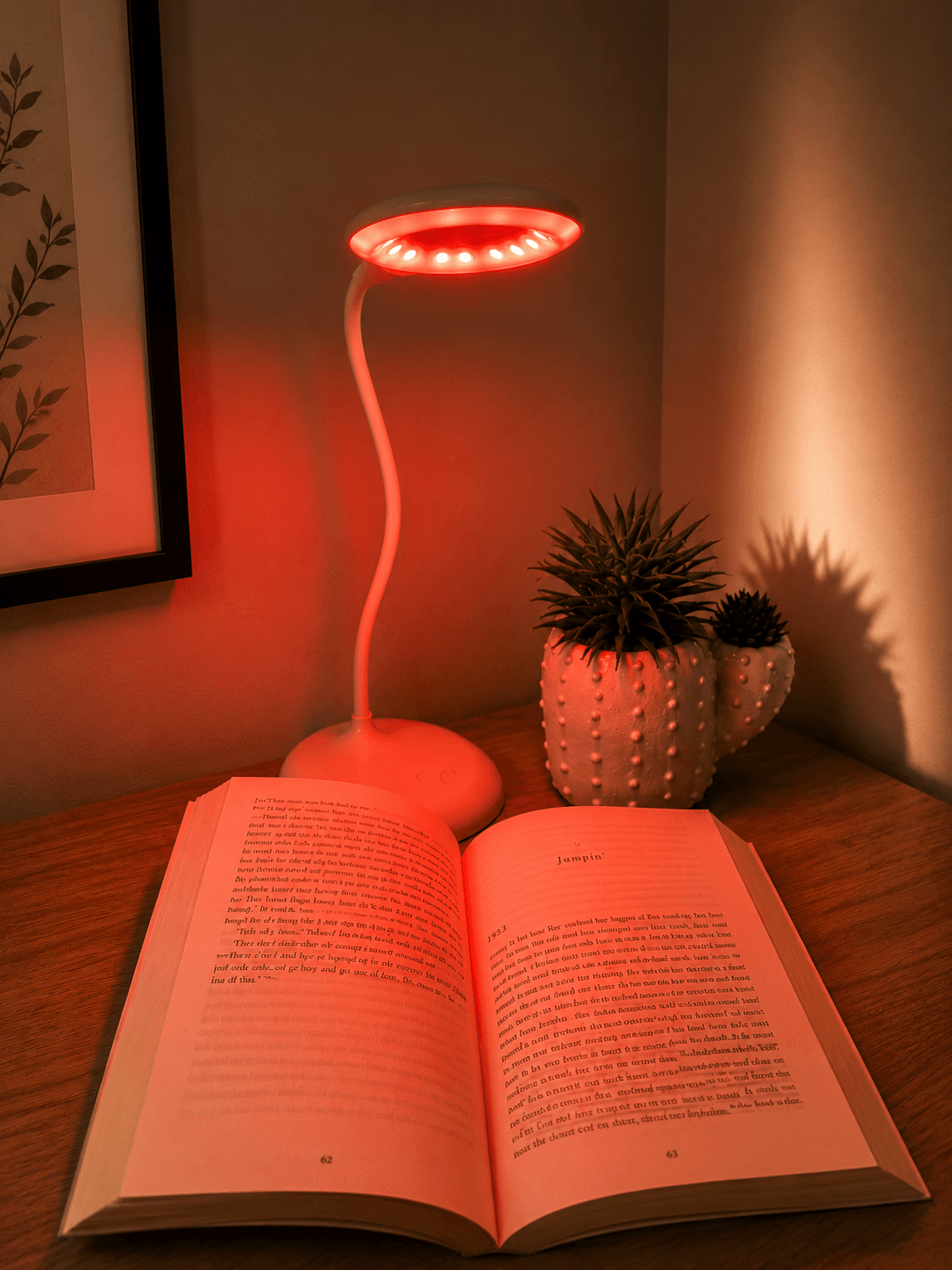 Dusk Eclipse red glowing sleep lamp with flexible neck illuminating open book on wooden table.