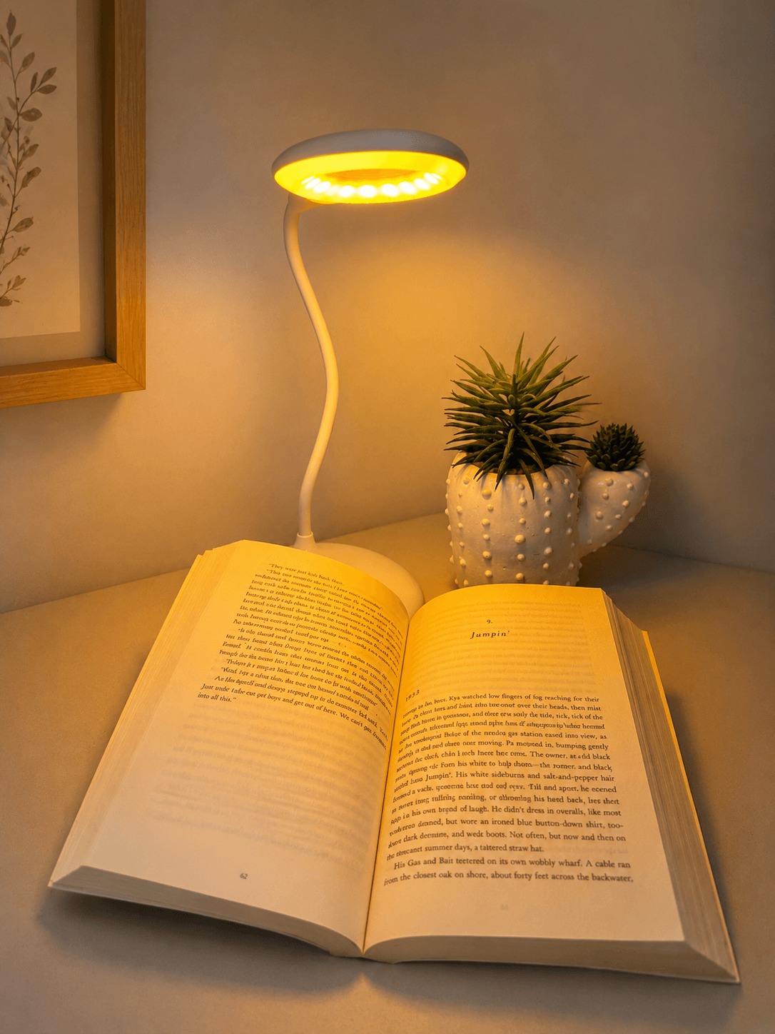 Flexible white Dusk Eclipse multi-mode sleep lamp casting warm light over an open book on a wooden surface, styled with a.
