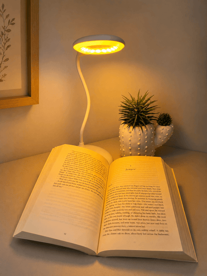 Flexible white Dusk Eclipse multi-mode sleep lamp casting warm light over an open book on a wooden surface, styled with a.