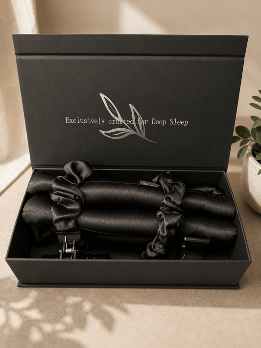 A black gift box with the lid open, displaying black silk heatless curler with scrunchies and hair clips inside. The inside lid is printed with the text 'Exclusively crafted for Deep Sleep' and a silver leaf logo.
