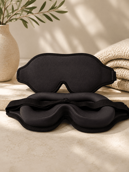Black contoured 3D sleep mask made of smooth mulberry silk with bluelight free and blackout sleep mask features, set on a beige.