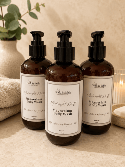Three amber pump bottles of Midnight Drift Magnesium Body Wash with natural beige labels on a neutral-toned surface,.